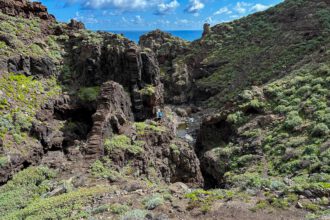 Wanderin im Barranco Anosma vor einem Felsenriegel mit Blick auf Barranco und den Atlantik