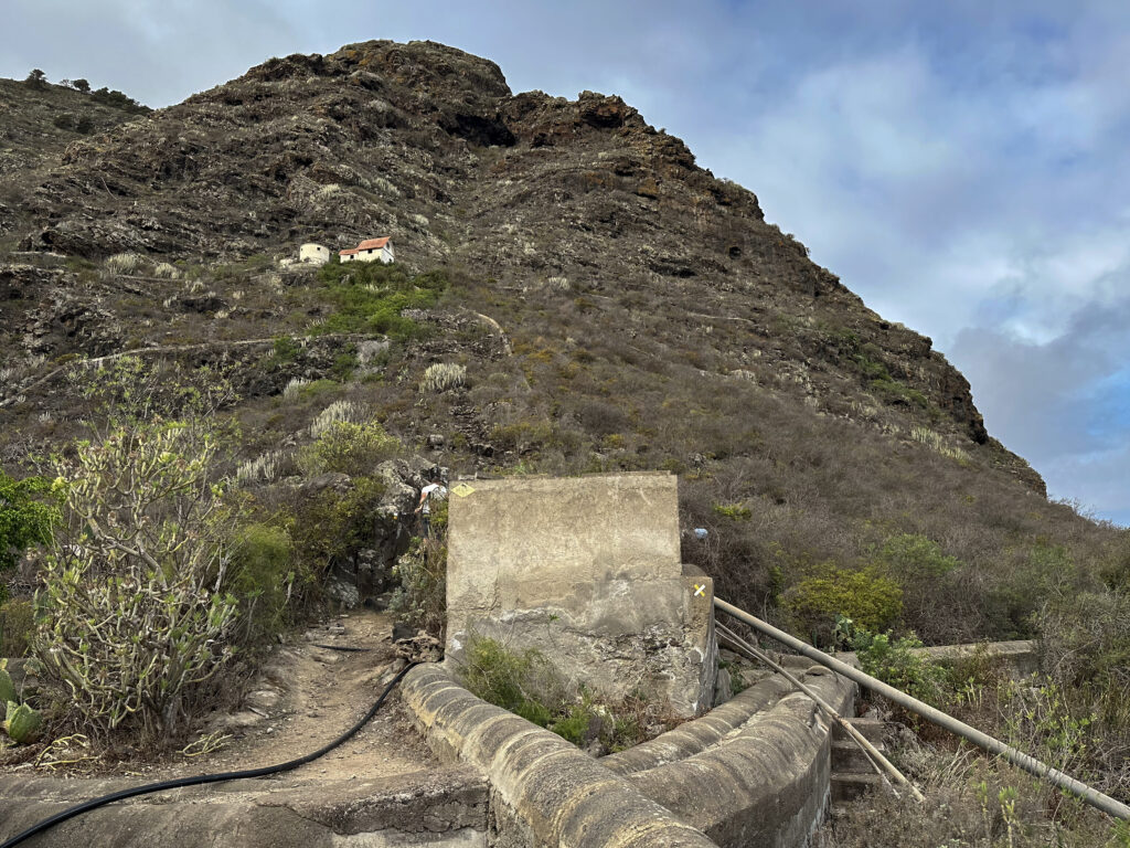 Ruta de senderismo más allá de una estación de bombeo de agua y edificios en el fondo, que ya te puedes ver desde la distancia en la ladera